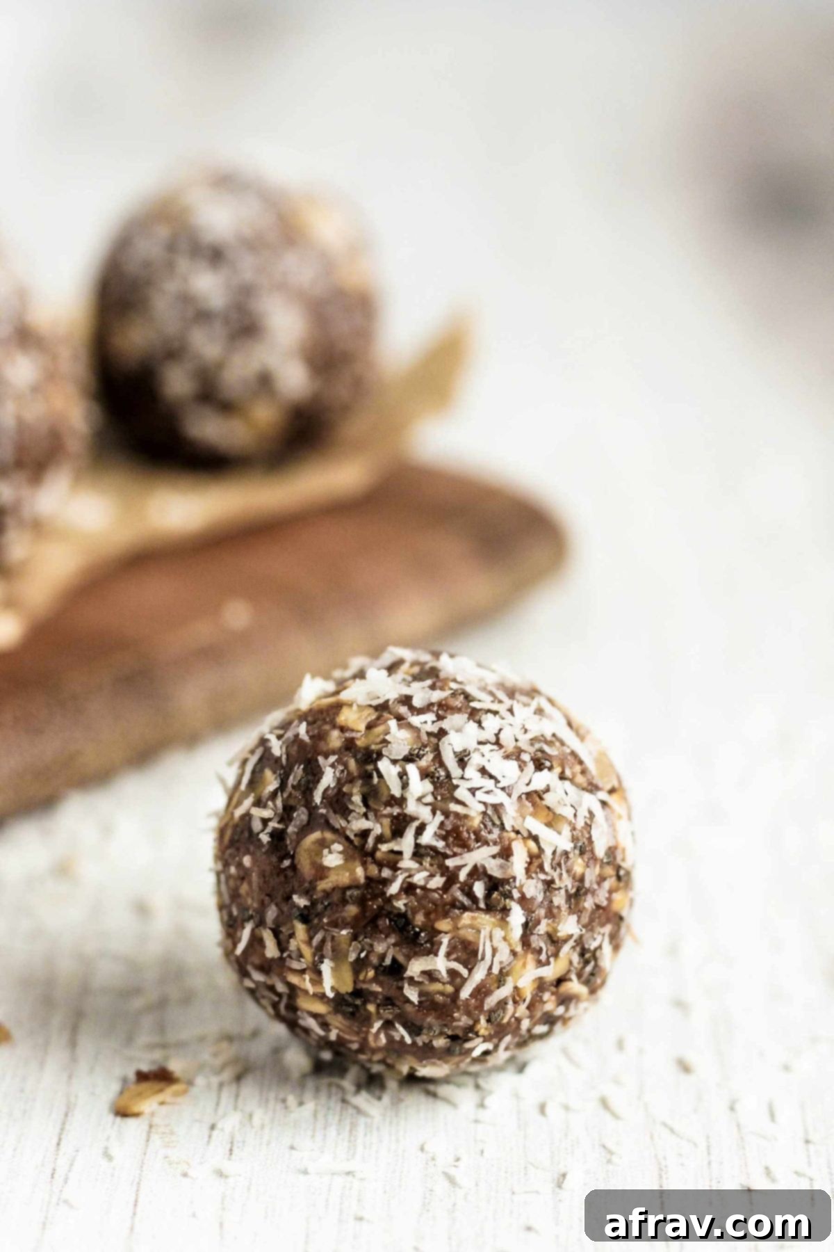 Chocolate Coconut Peanut Butter Balls 9 A single chocolate coconut peanut butter energy ball on a white board with more snacks in the background.
