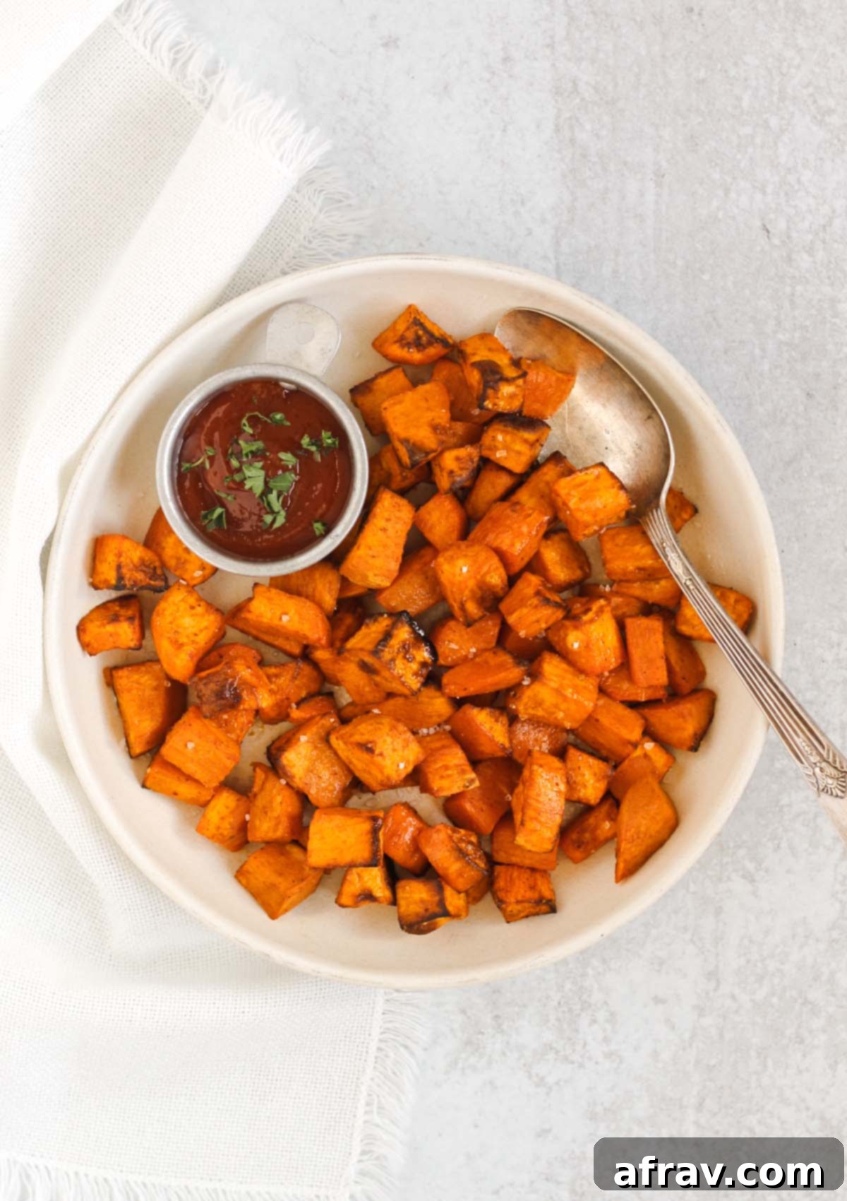 Air fried sweet potato cubes with a vintage serving spoon and side of ketchup on a round cream plate.
