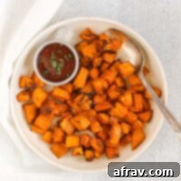 Air fried sweet potato cubes with a vintage serving spoon and side of ketchup on a round cream plate.