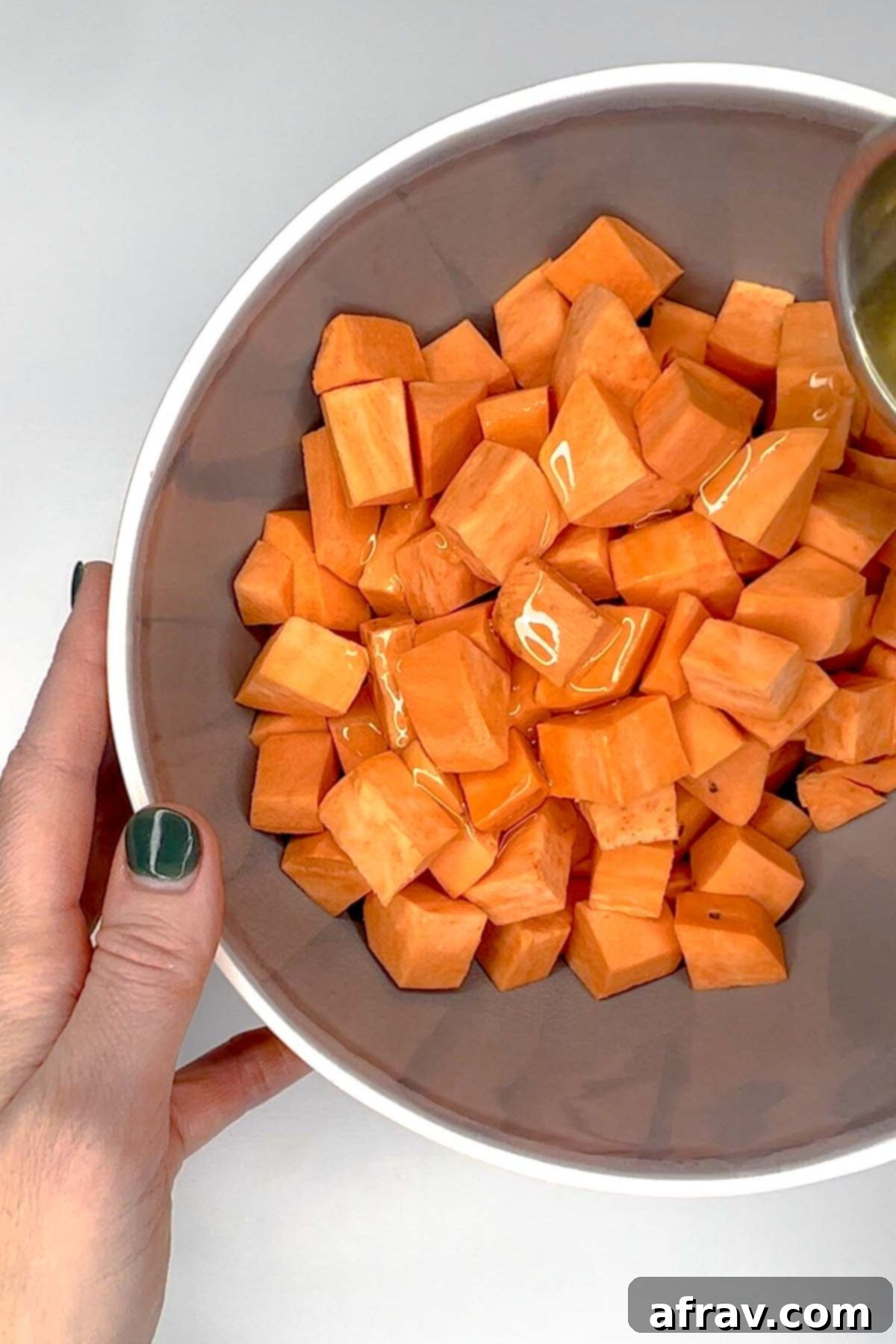 Sweet potato cubes in a gray mixing bowl with oil drizzled on top.