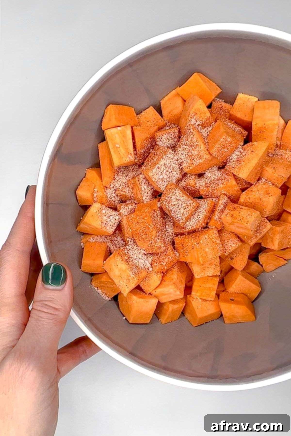 Sweet potato cubes sprinkled with seasoning in a gray mixing bowl.