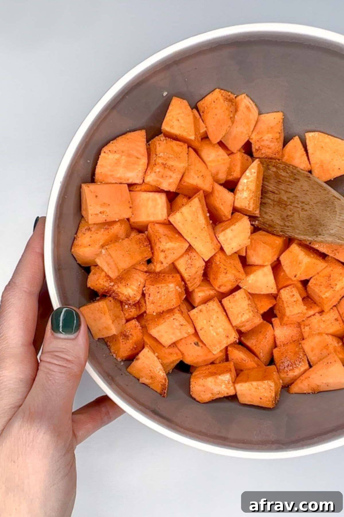 Sweet potato cubes mixed with seasoning in a gray mixing bowl.