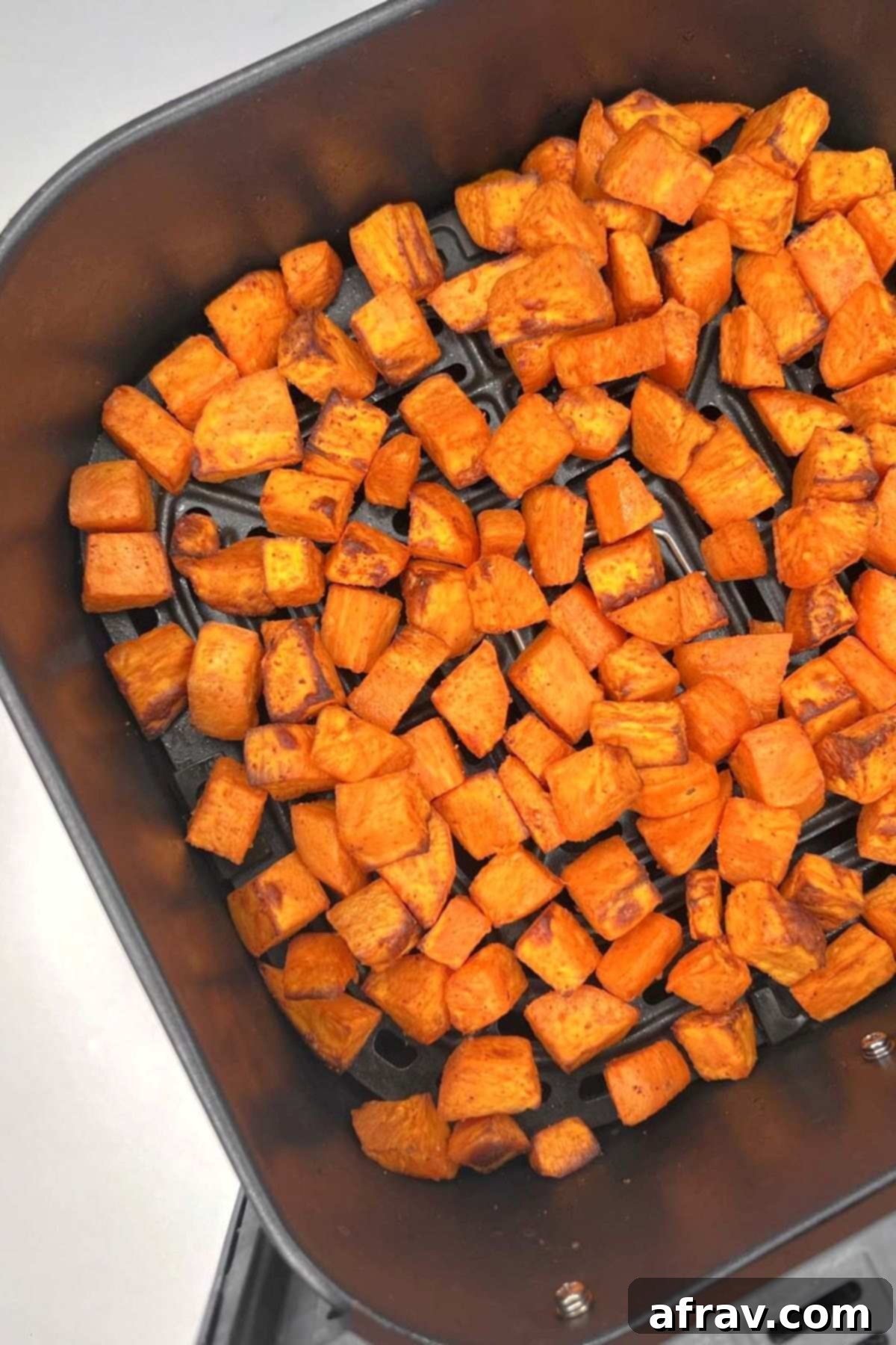 Cooked sweet potato cubes in an air fryer basket.