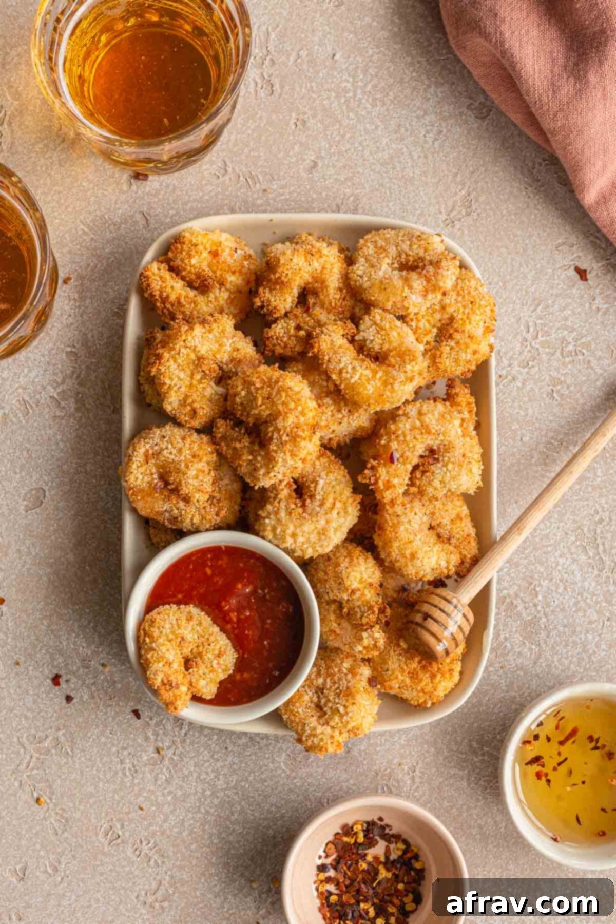 Air fryer breaded shrimp piled on a rectangular plate with bowls of seafood sauce and honey in view.