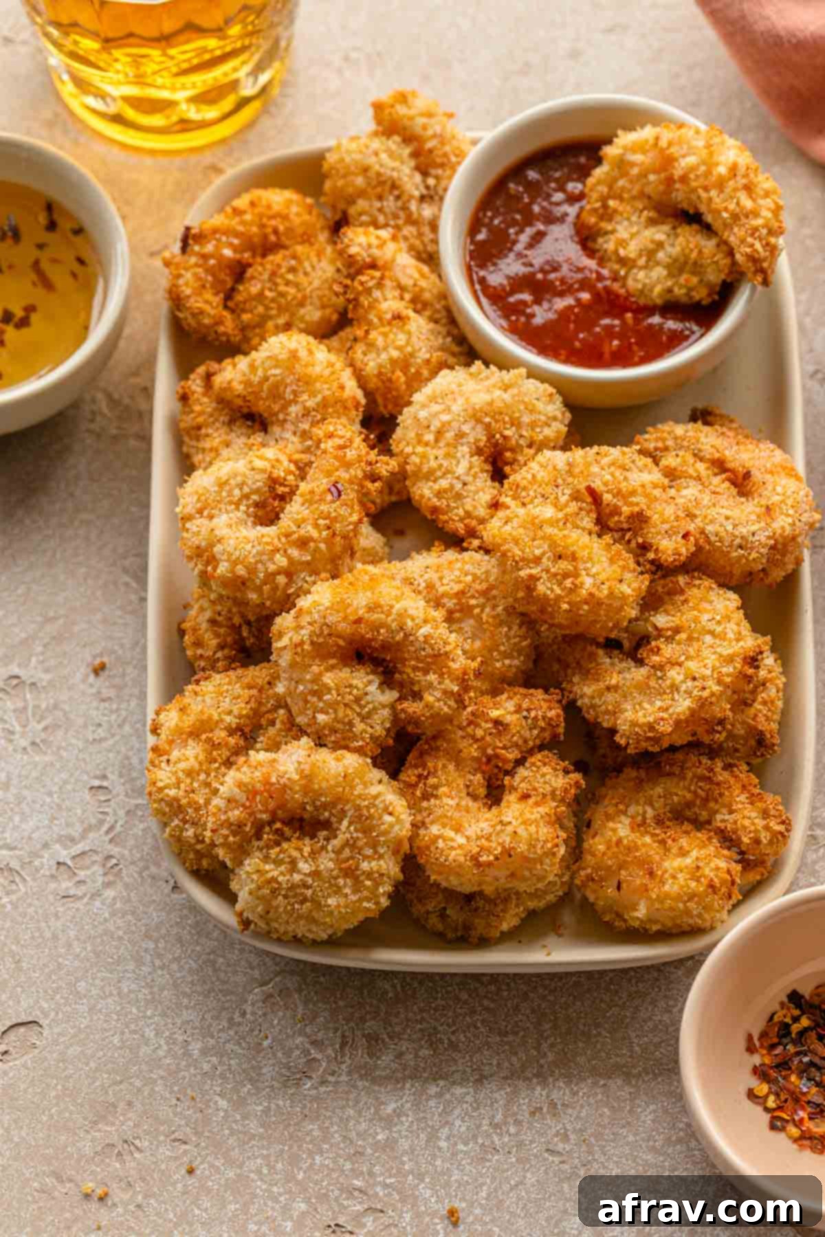 Close up of crispy breaded shrimp on a plate with seafood sauce in the background.