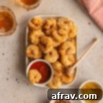 Overhead view of air fryer breaded shrimp on a plate with seafood sauce and a wooden honey dipper.