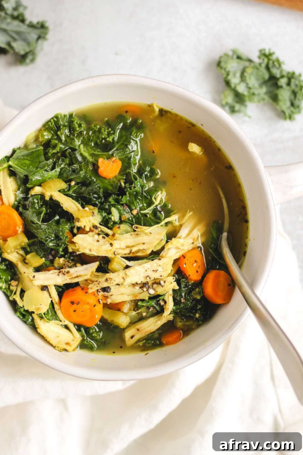 Chicken and kale soup in a white soup bowl with a spoon.