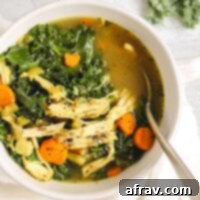 Chicken and kale soup in a white soup bowl with a spoon.