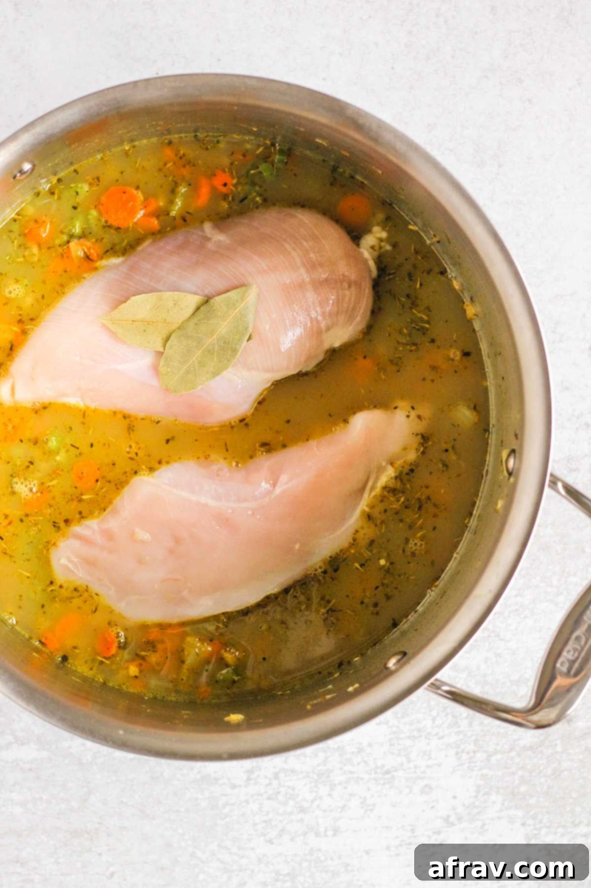 Broth and chicken soup ingredients in a large stock pot with raw chicken breasts.