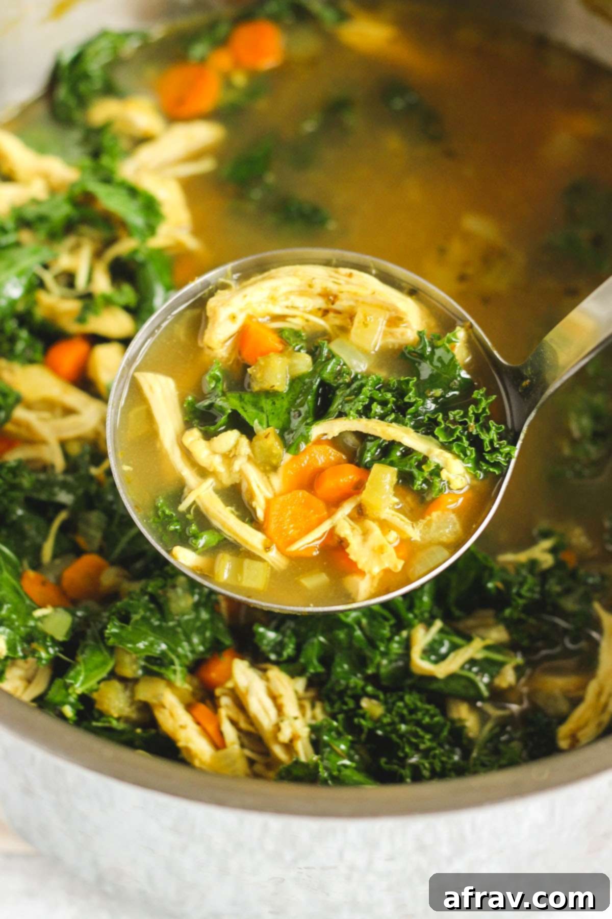 Soup ladle scooping chicken and kale soup from a stock pot.