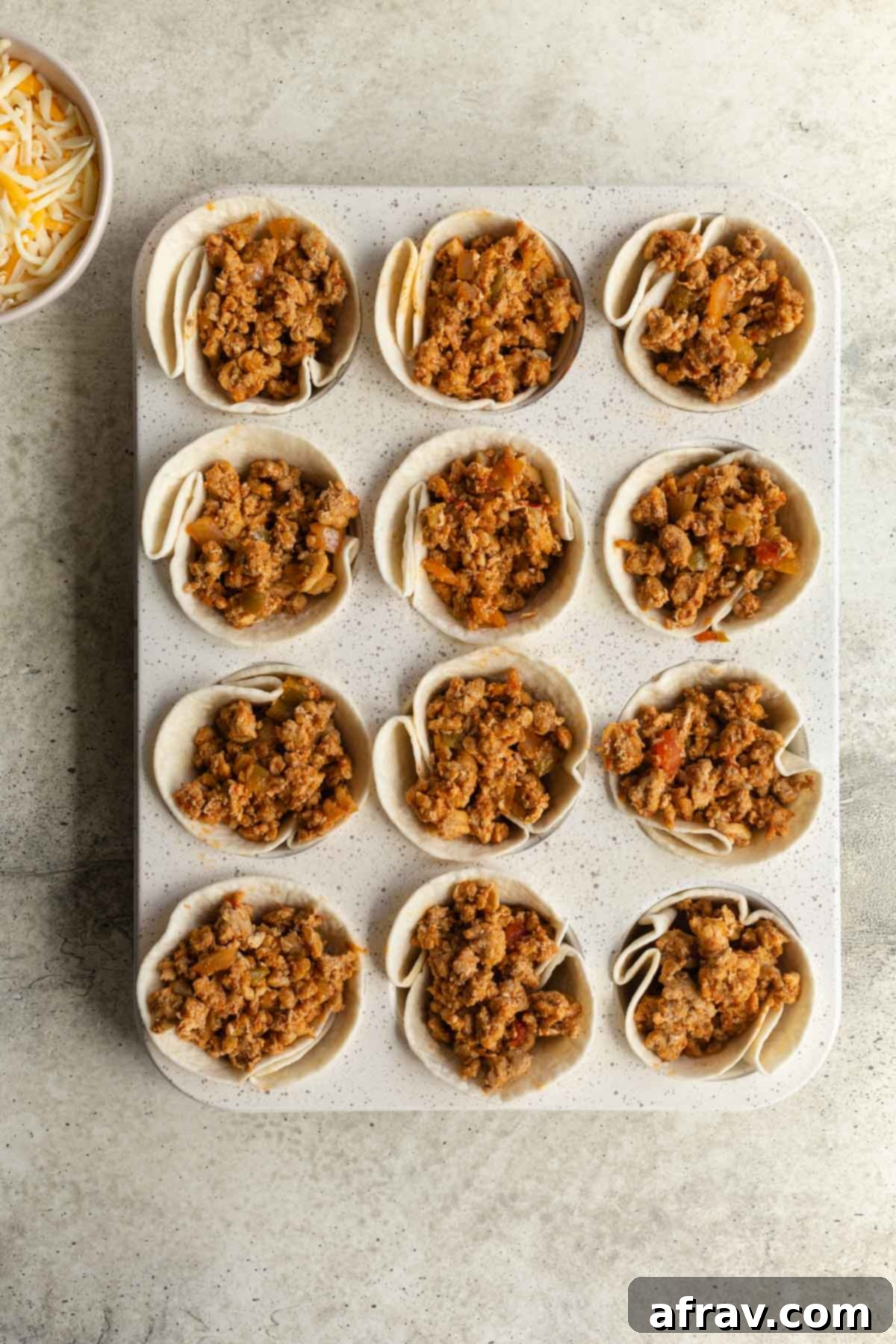A hand carefully pressing a mini tortilla into a greased muffin tin cavity to form a cup shape.