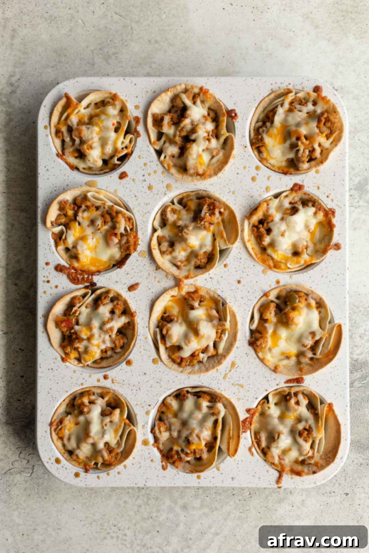 A muffin pan filled with ground turkey taco cups, each generously topped with shredded cheese and ready to be baked.