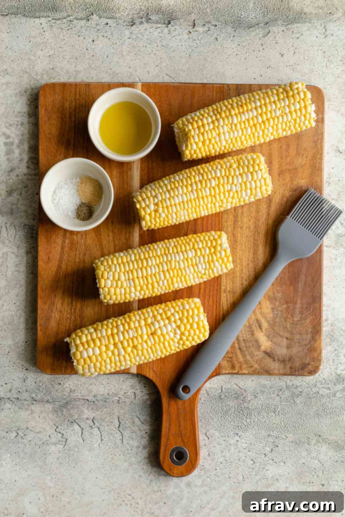 Ingredients to make air fryer corn on the cob arranged on a wooden cutting board.