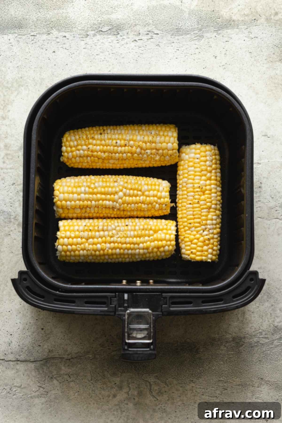 Four ears of raw, fresh corn arranged in an air fryer basket.