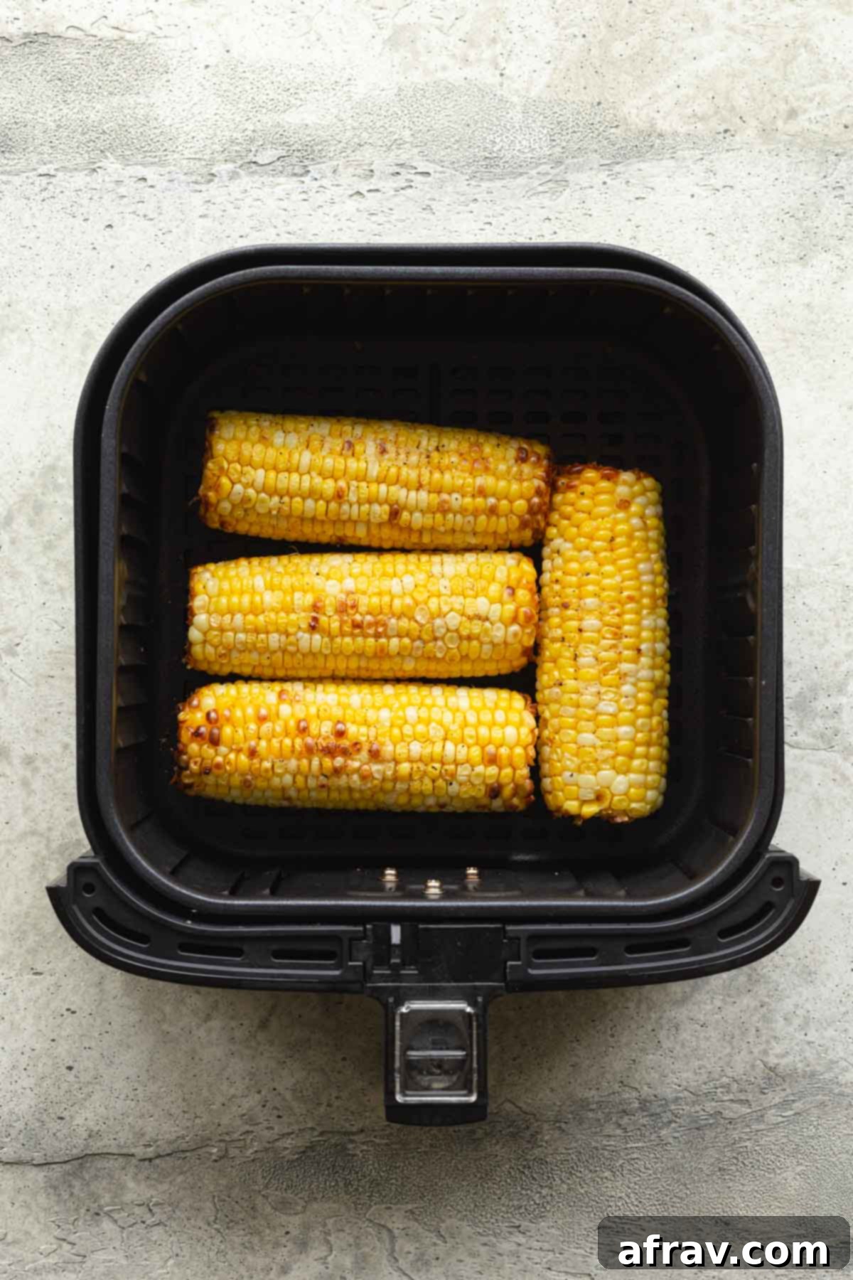 Four ears of fully cooked corn in an air fryer basket.