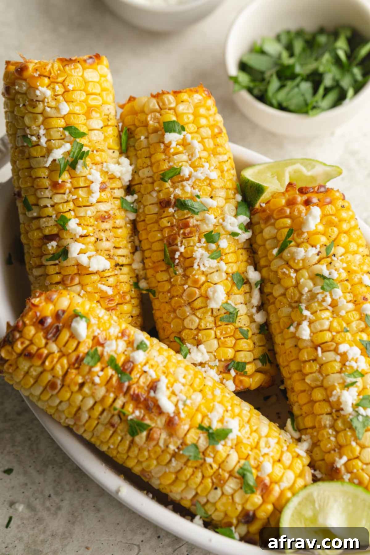 Corn on the cob in a white dish and topped with parsley and feta.