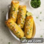 Four ears of air fried corn in a white dish and topped with feta and parsley.