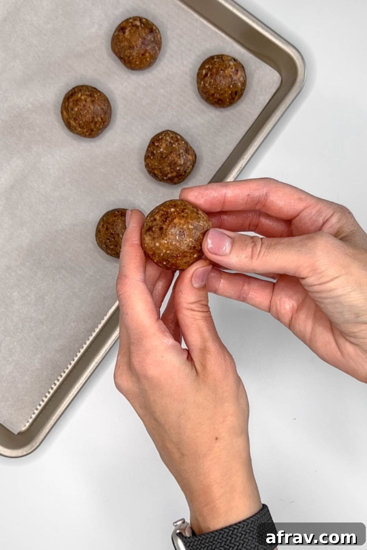 Two hands rolling a carrot cake energy bite.