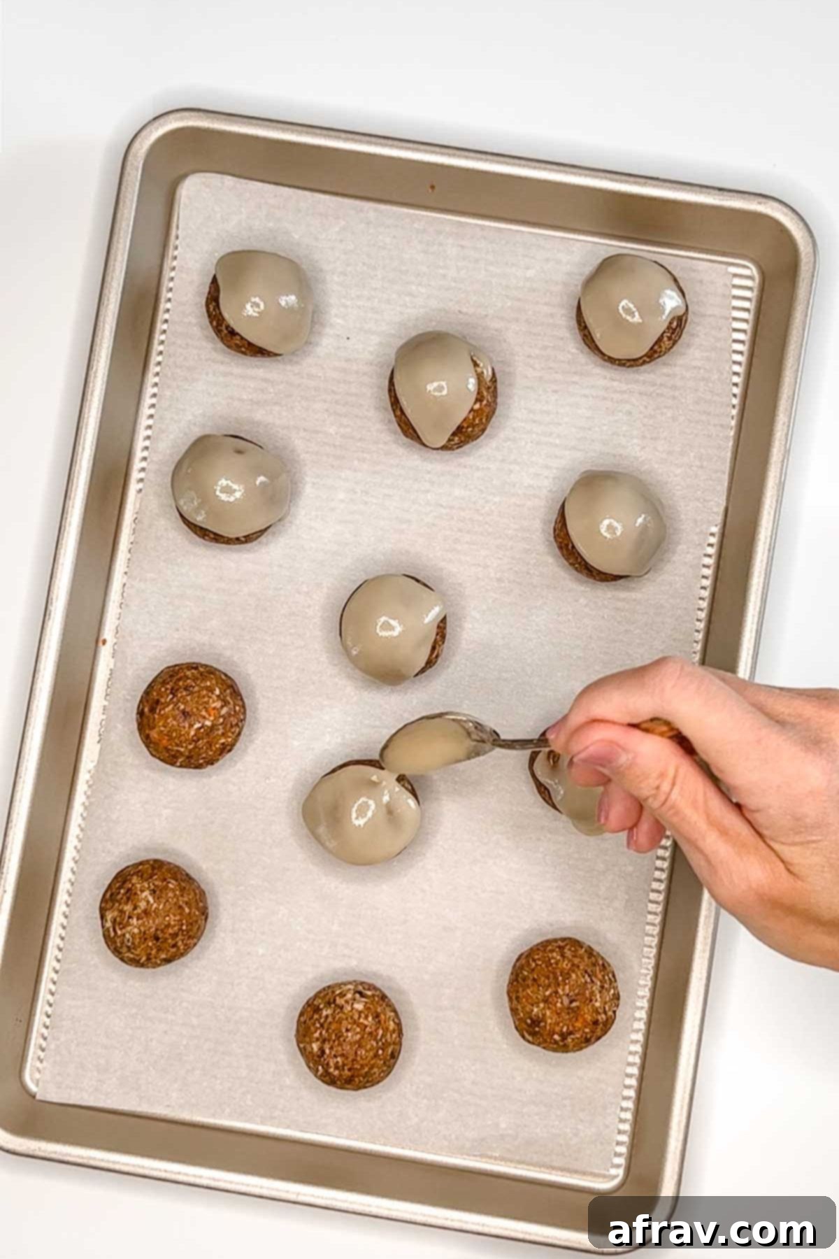 A hand holding a spoon drizzling glaze over carrot cake balls.