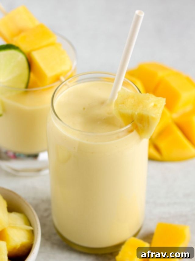 Tropical Mango Pineapple Blend 2 Mango pineapple smoothie in a tall glass with a paper straw and a small glass filled with mango/pineapple smoothie in the foreground.