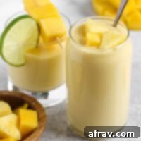 Tropical Mango Pineapple Blend 7 Two glasses filled with a creamy yellow smoothie topped with fresh pineapple and mangos.