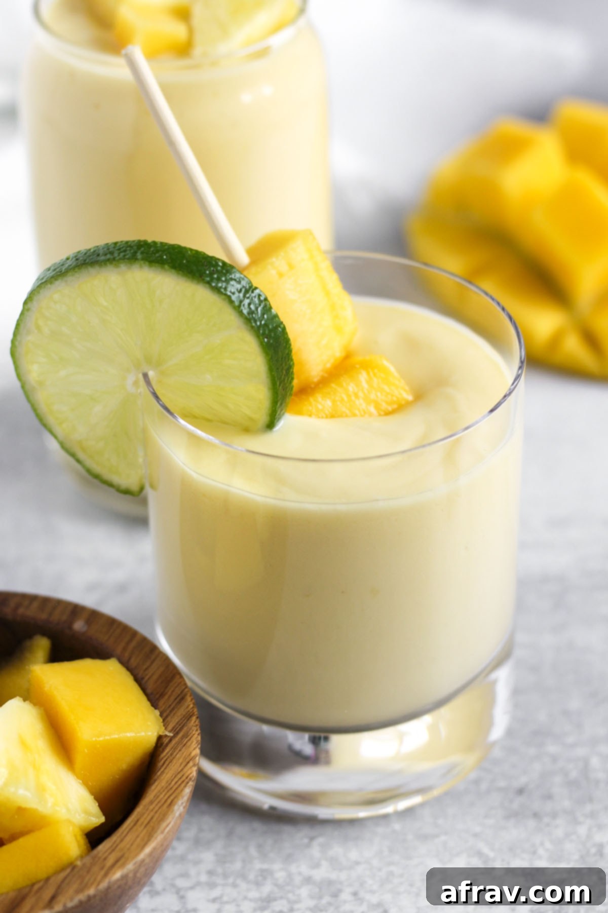 Tropical Mango Pineapple Blend 6 Creamy yellow smoothie in a short glass with a lime slice on the rim and mango chunks topping the smoothie.