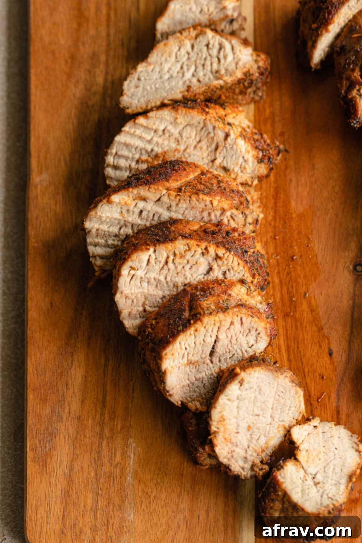Perfect Air Fryer Pork Tenderloin 2 Close up view of pork tenderloin slices on a wooden board, showcasing its tender texture and delicious crust.