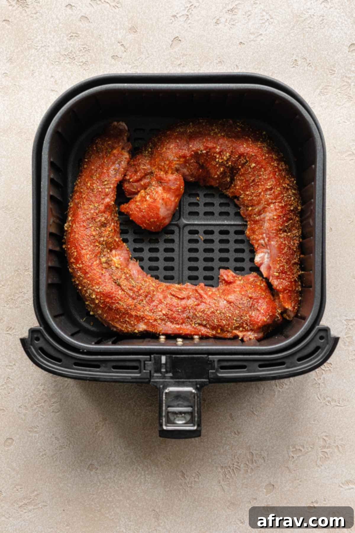 Perfect Air Fryer Pork Tenderloin 6 Two seasoned pork tenderloins perfectly placed in an air fryer basket, ready to be cooked.