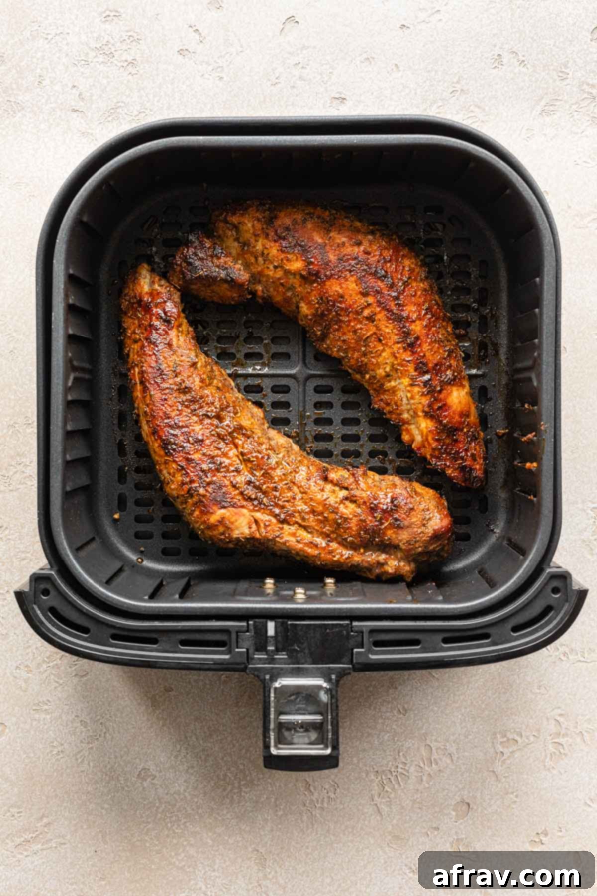 Perfect Air Fryer Pork Tenderloin 7 Two cooked pork tenderloins inside an air fryer basket, perfectly browned and ready for resting.