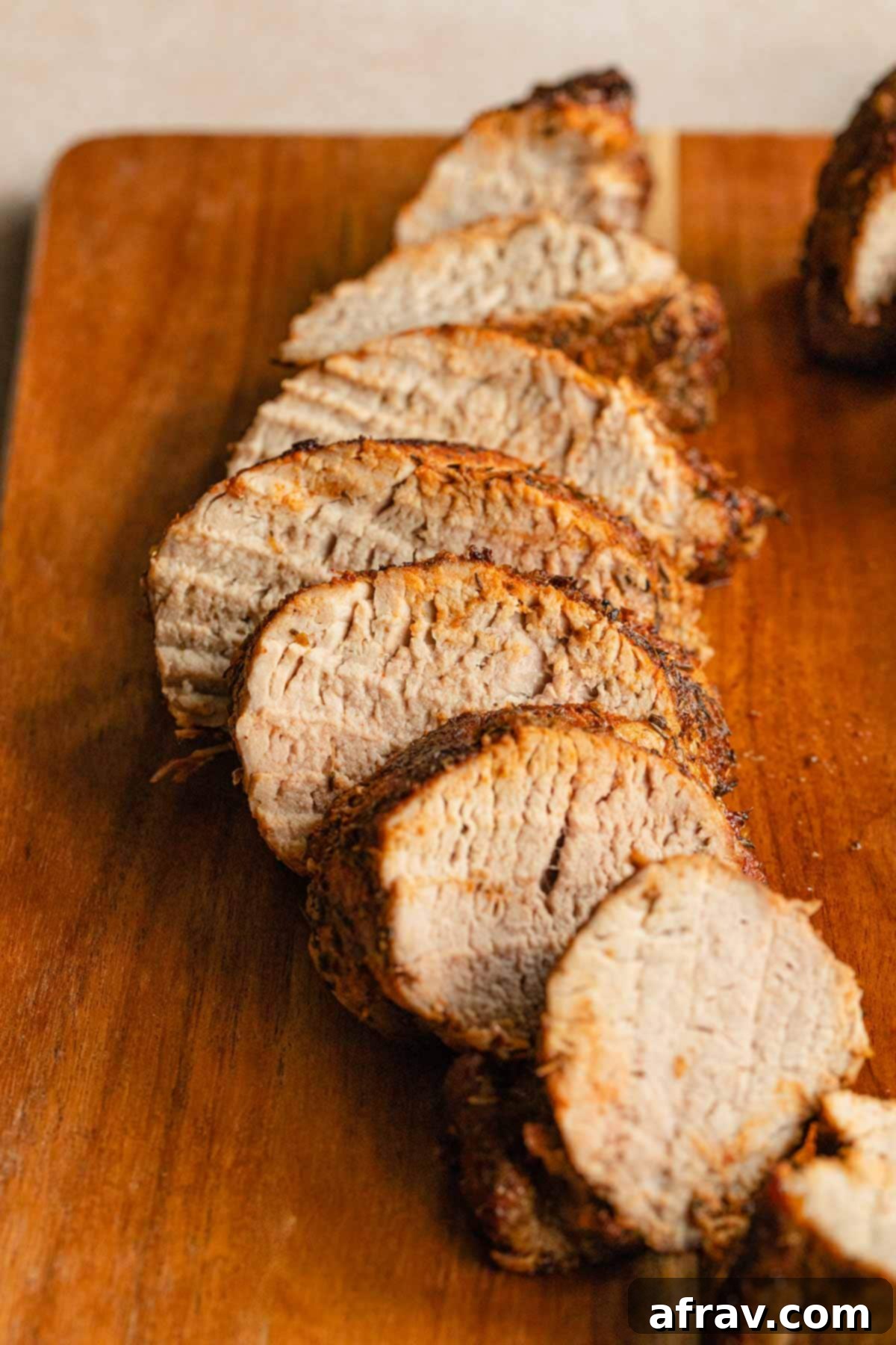 Perfect Air Fryer Pork Tenderloin 9 Side view of perfectly cooked and sliced pork tenderloin on a wooden cutting board, garnished lightly.