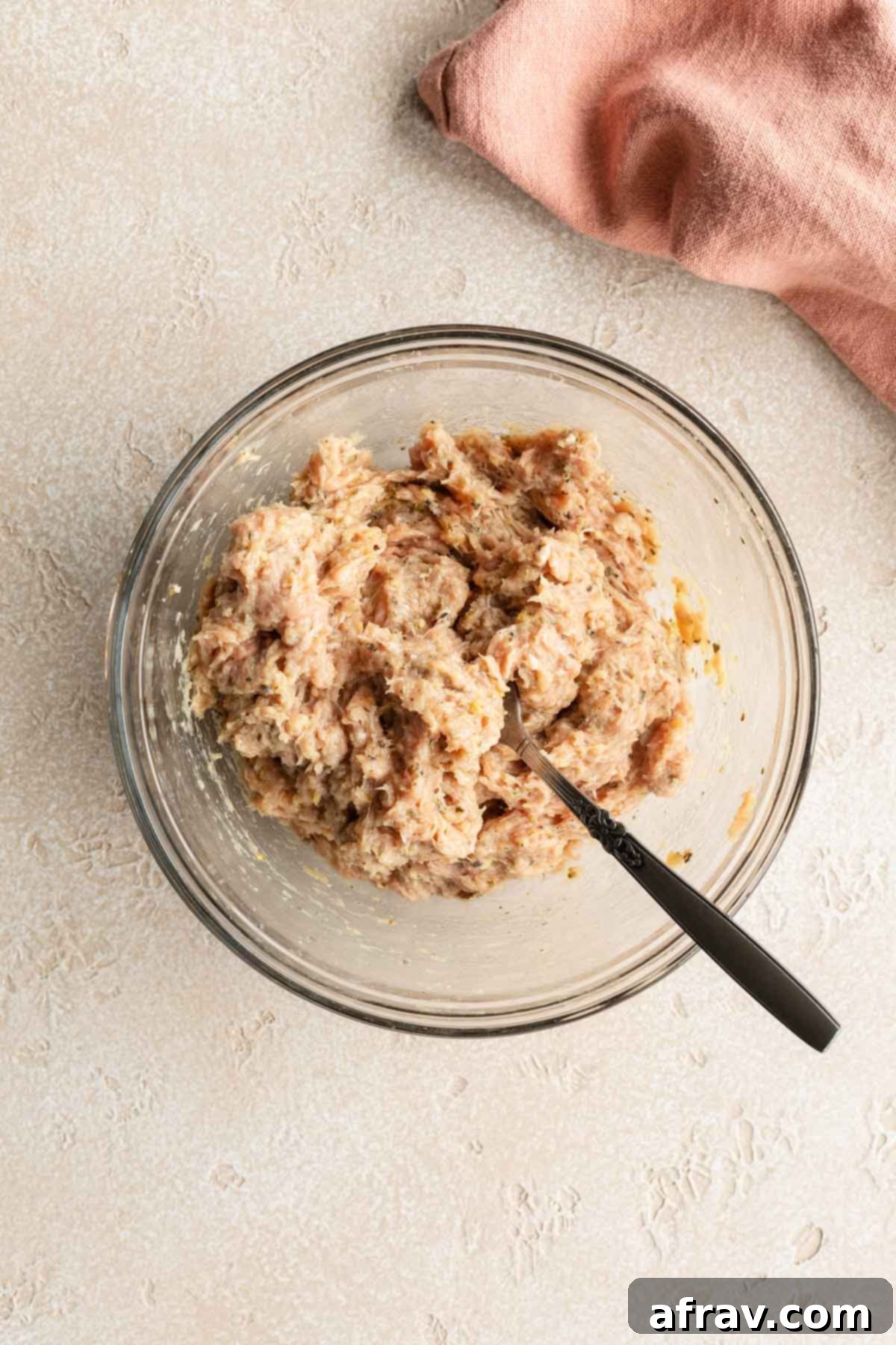 Burger ingredients mixed together in a glass bowl with a fork.