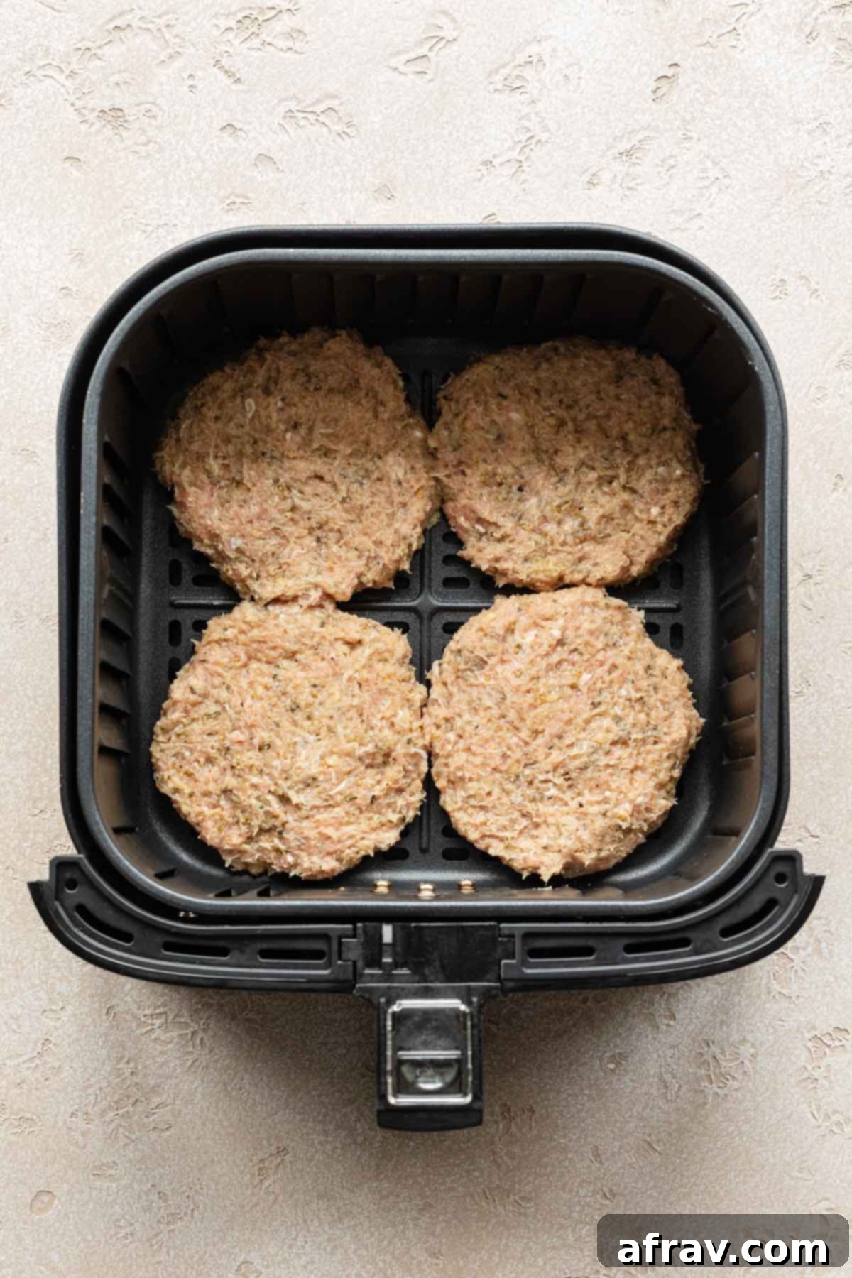 Four turkey burger patties in an air fryer basket.