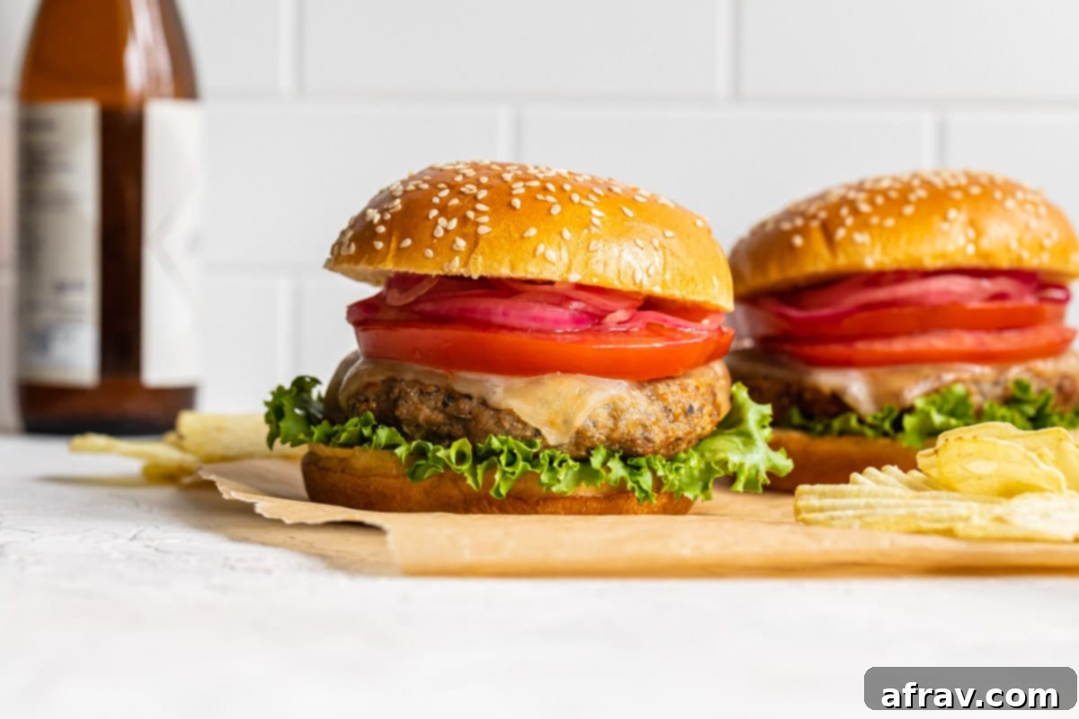 Side view of two turkey burgers on brown parchment paper with potato chips.