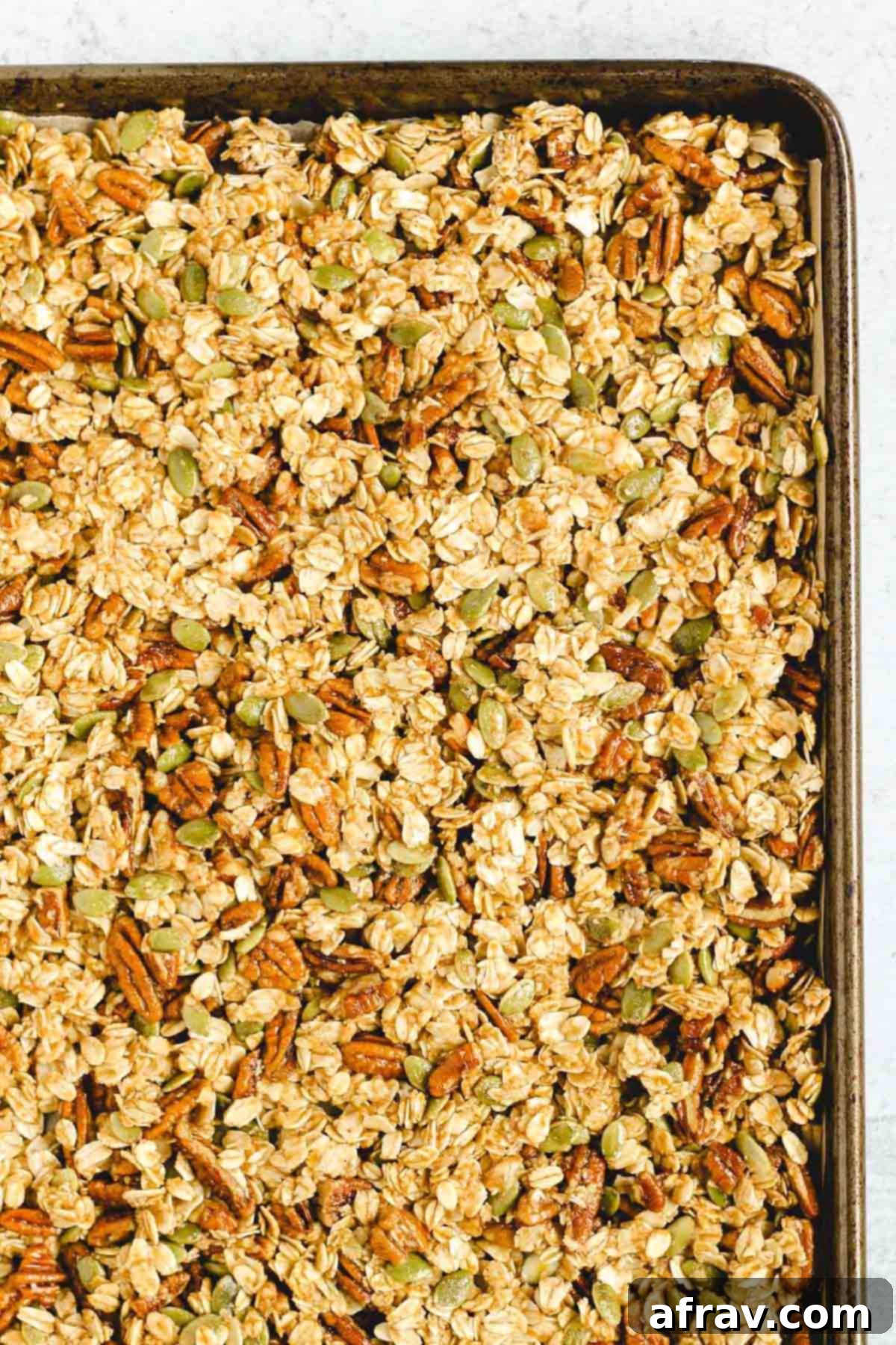 Wholesome Pumpkin Crunch Granola Gluten Free Plant Based 5 Pumpkin granola mixture spread evenly across a baking sheet lined with parchment paper, before being placed in the oven.