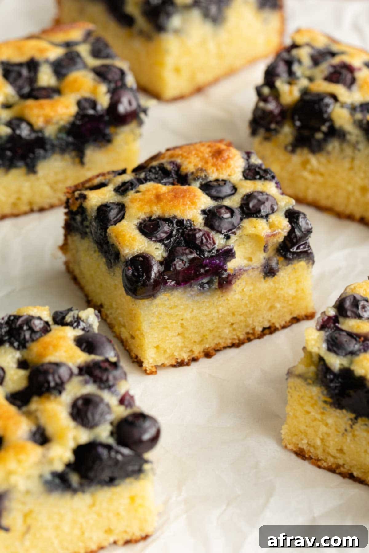 Lemon blueberry cake cut into squares and arranged on a sheet of parchment paper, showcasing its moist texture.