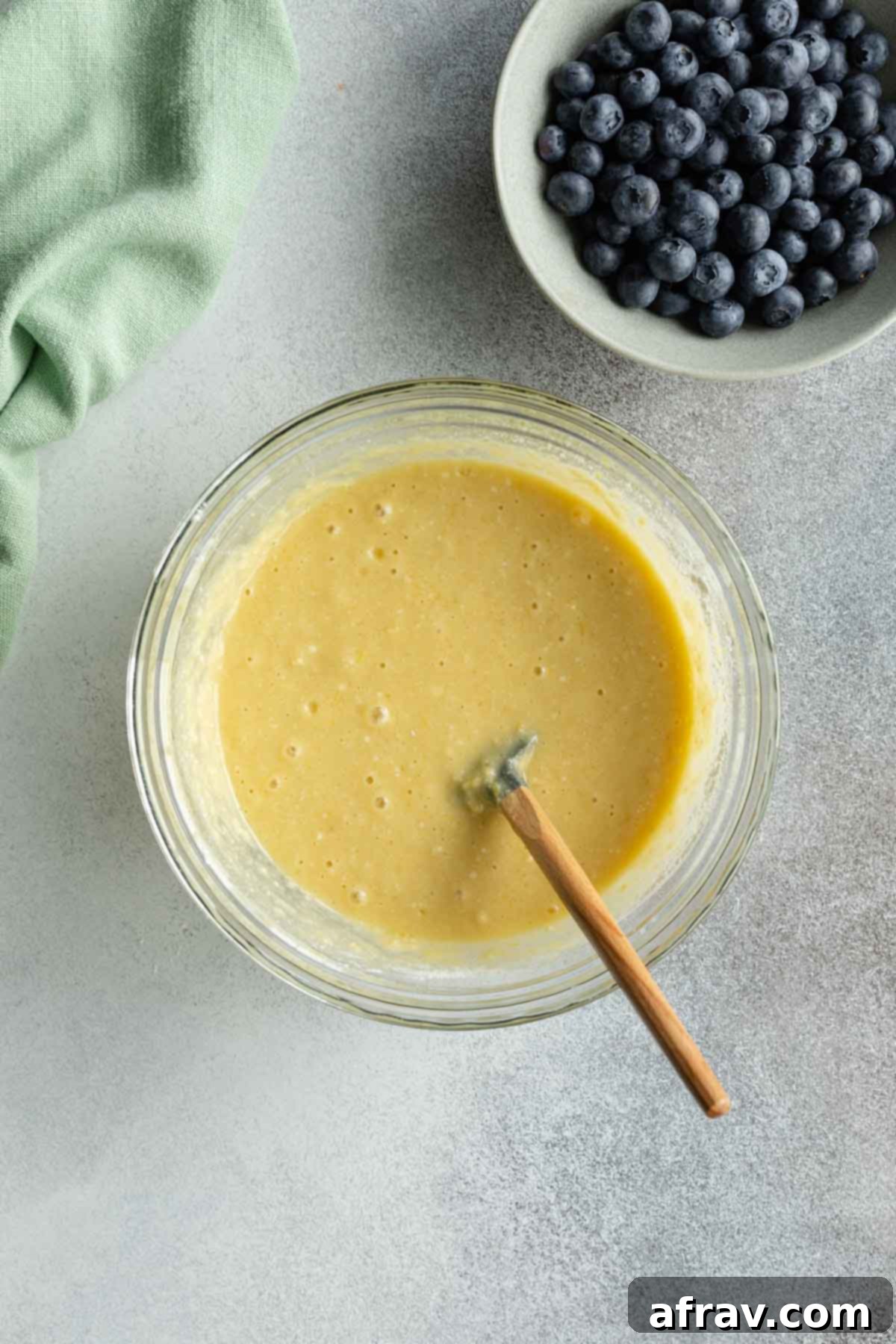 Blueberry cake batter in a glass bowl with a spatula, showing the combined wet and dry ingredients.
