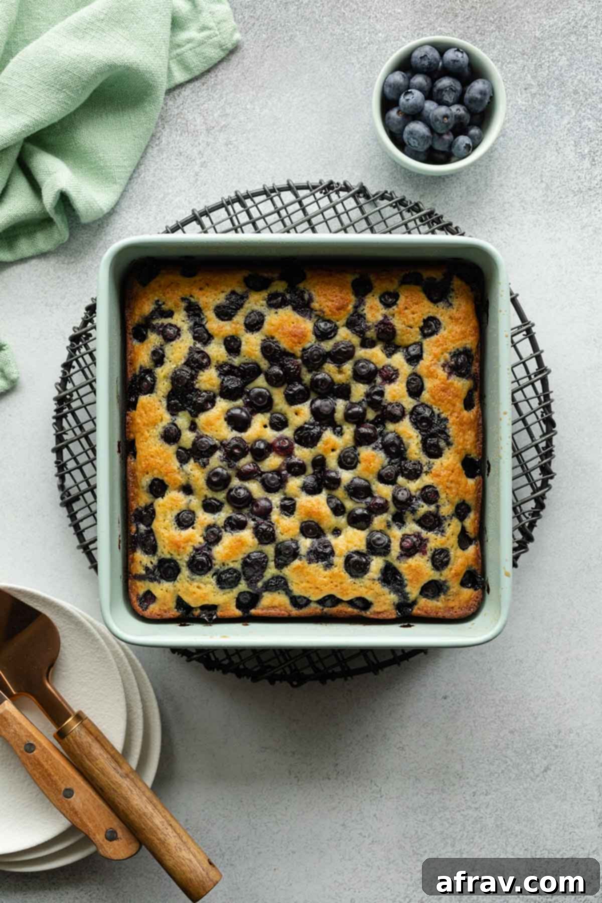 Overhead view of blueberry cake cooling on a wire rack, ready to be sliced.