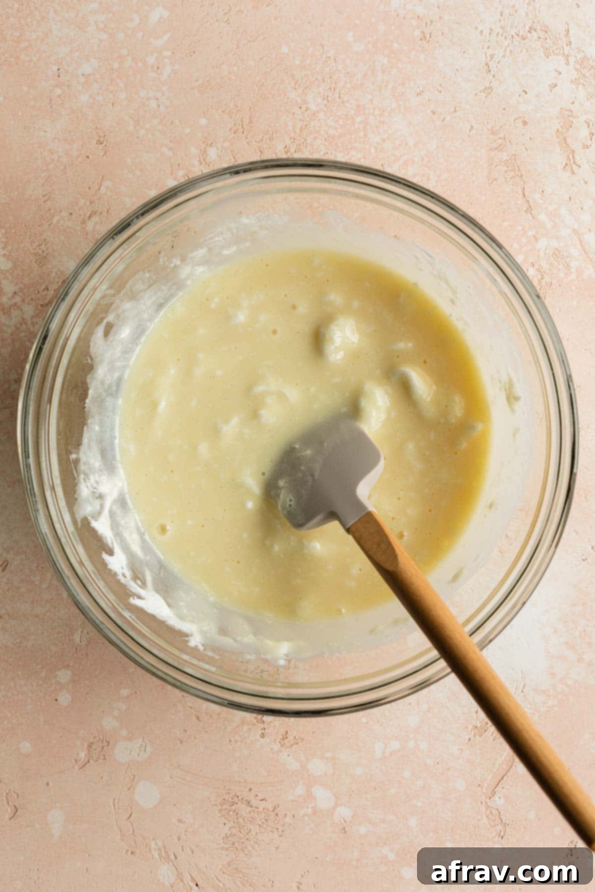 Melted marshmallows and condensed milk stirred together in a glass bowl with a spatula.