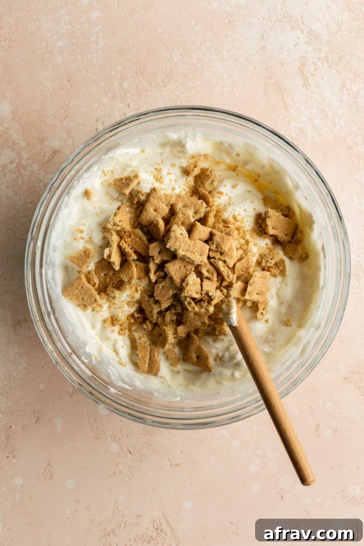 Chopped graham crackers added to the ice cream mixture in a glass bowl.