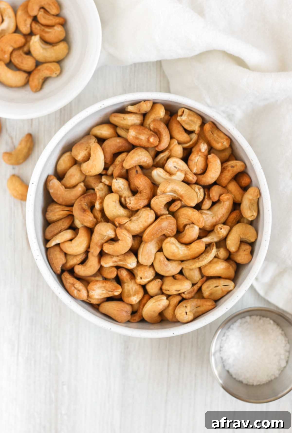Roasted cashews in a bowl with small bowls of cashews and sea salt off to the side.