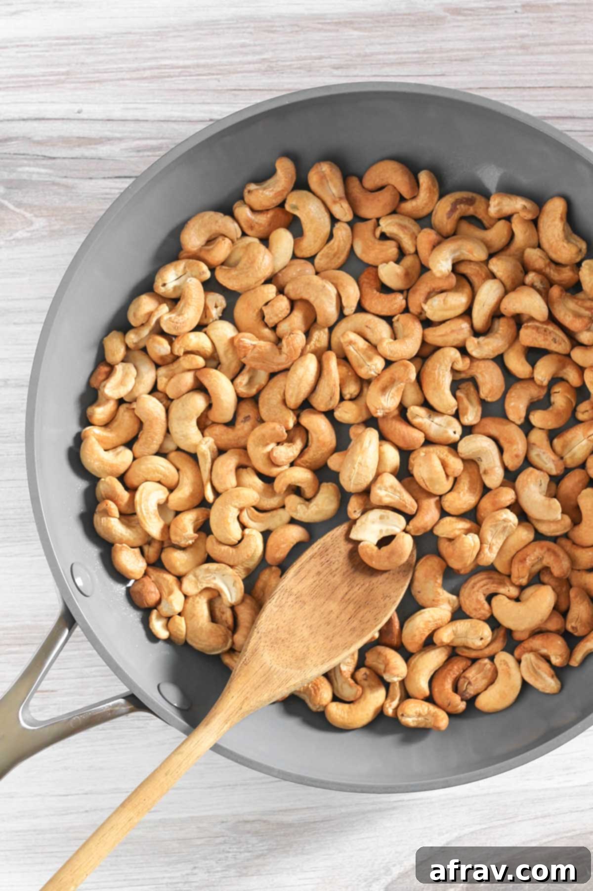 Toasted cashews in a frying pan with a wooden spoon.