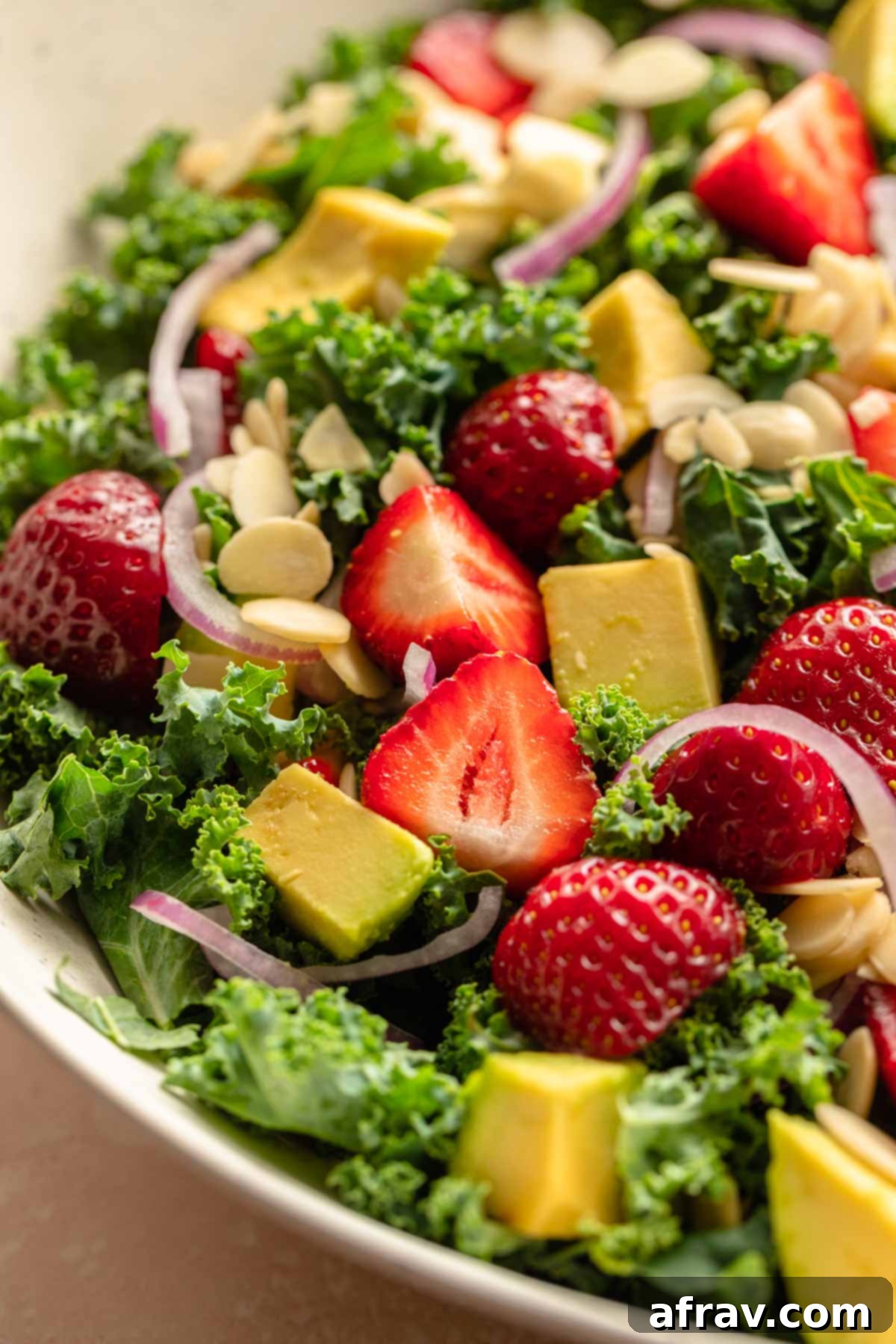 Vibrant Strawberry Kale Salad 5 Close up of chopped strawberries and avocado on top of a kale salad, ready to be tossed.