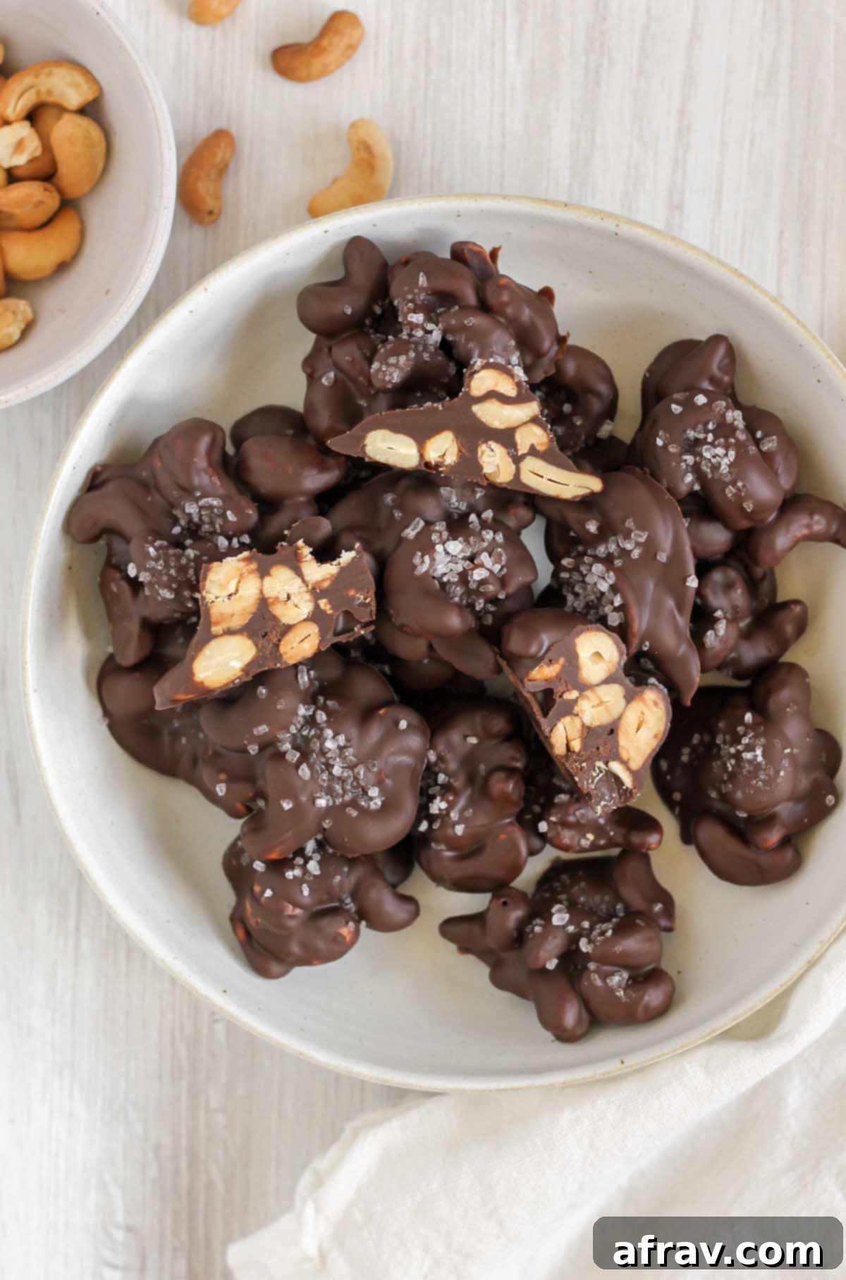 Overhead view of chocolate cashew clusters on a plate. Some cashew clusters cut in half to show center.