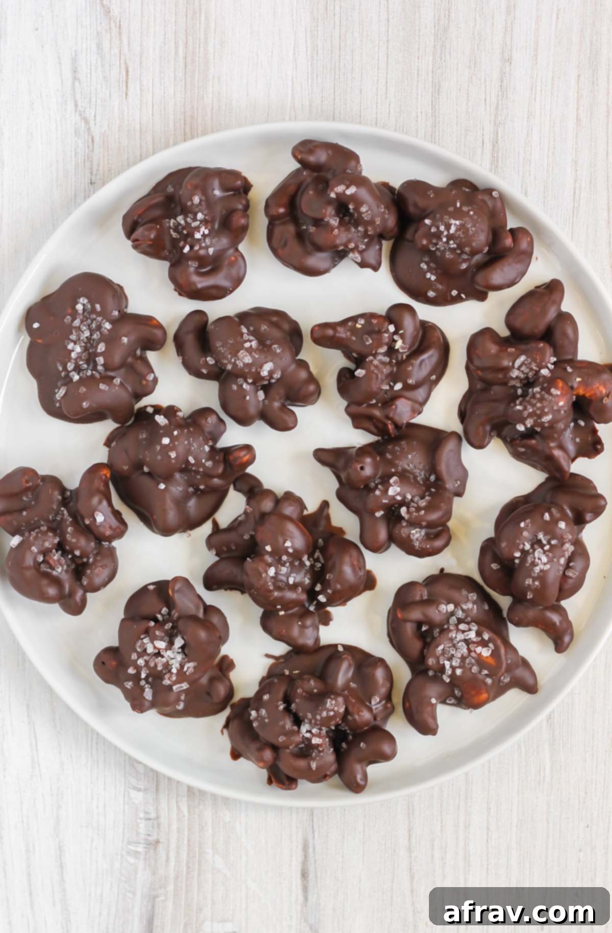 Chocolate covered cashew clusters topped with sea salt on a round white plate.