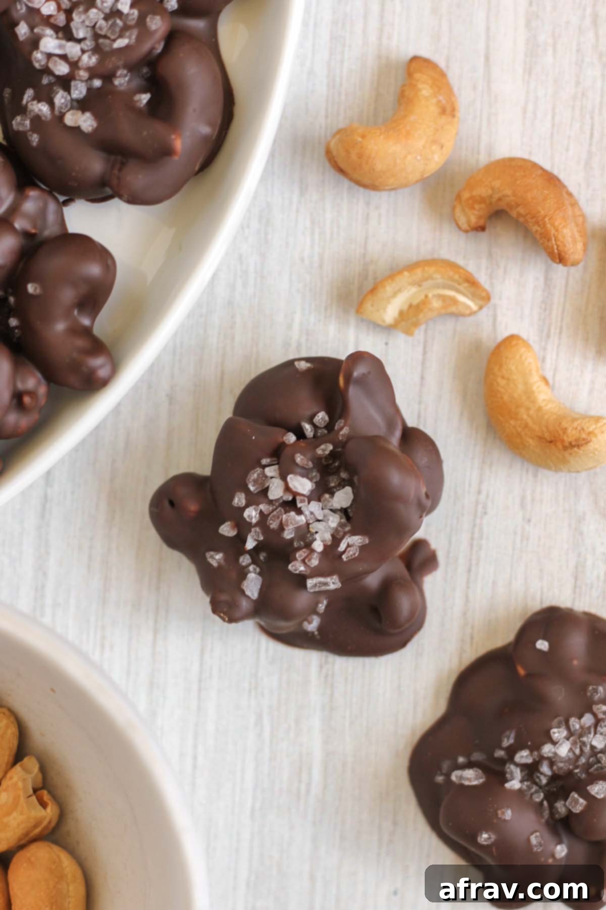 Close-up of chocolate cashew cluster with raw cashews sprinkled on the side.