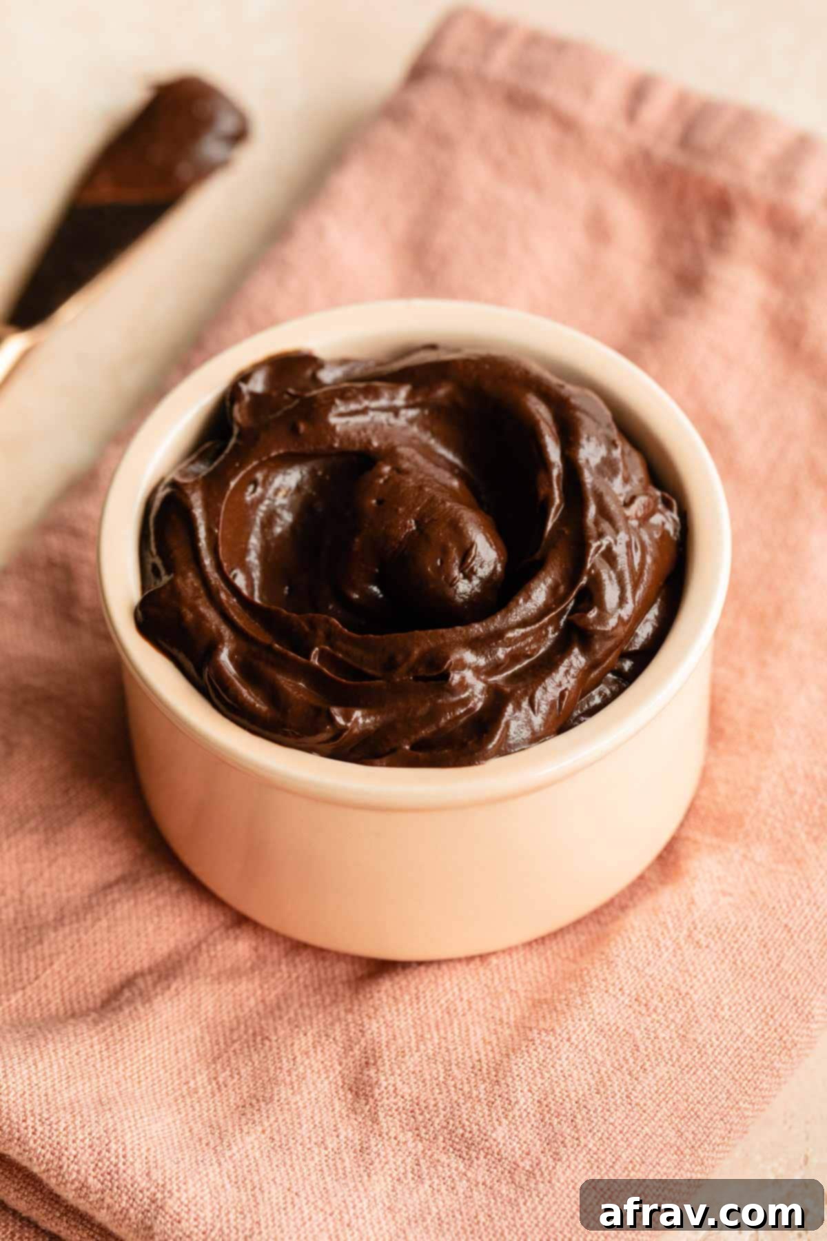 A vibrant pink dish filled with rich, dark chocolate avocado frosting, resting on a soft pink napkin, ready to be enjoyed.