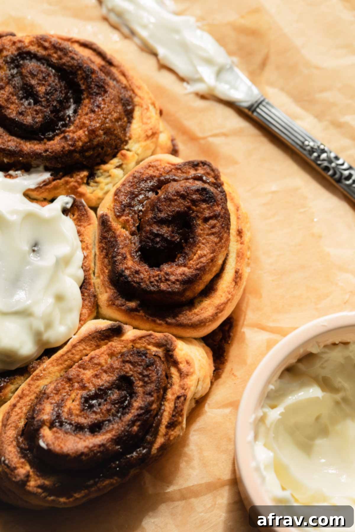Close-up overhead shot of air fryer cinnamon rolls with a golden crust and visible cinnamon swirls, resting on parchment paper.