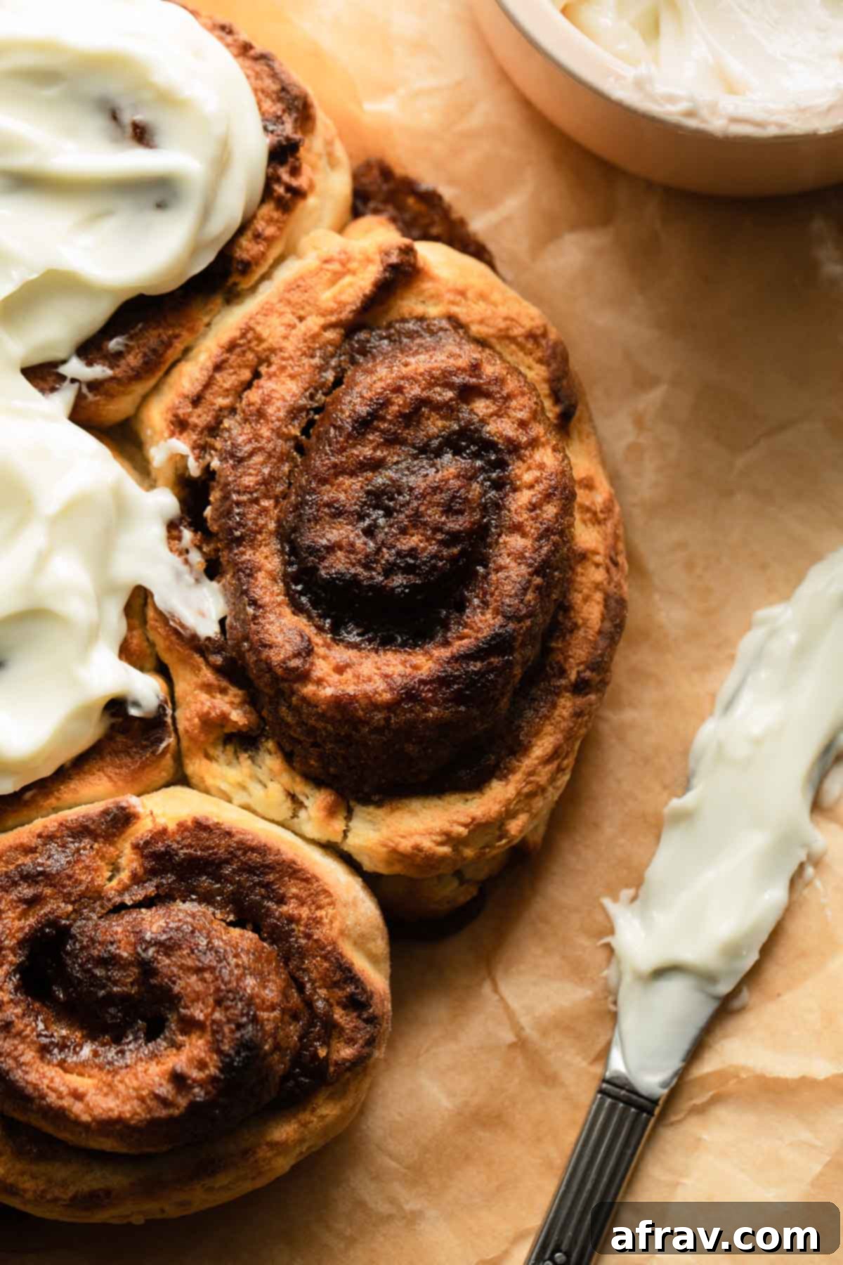 Close-up of a single air fryer cinnamon roll, perfectly frosted, with a knife on the side.