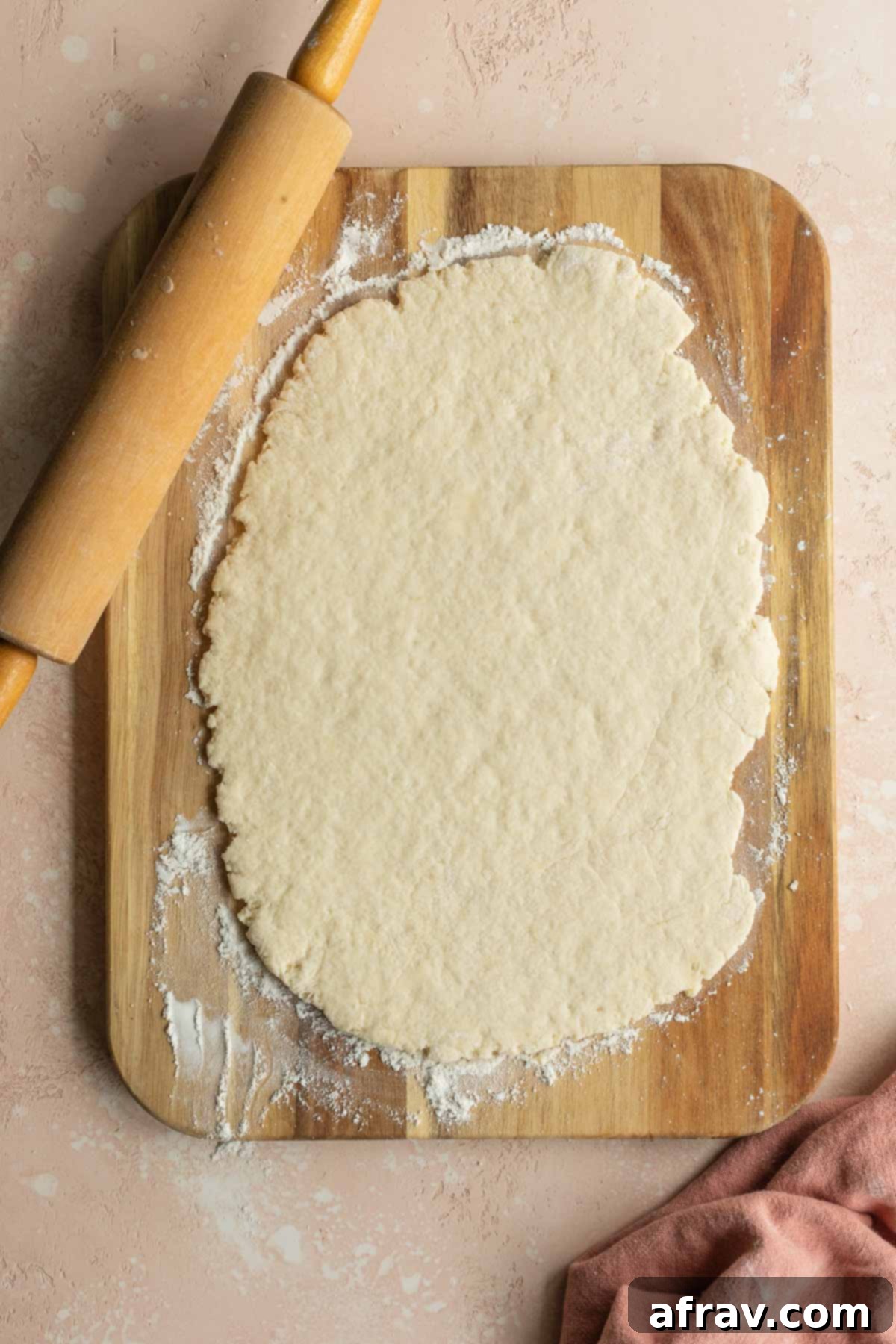 Rolled out cinnamon roll dough on a wooden board next to a rolling pin, ready for filling.