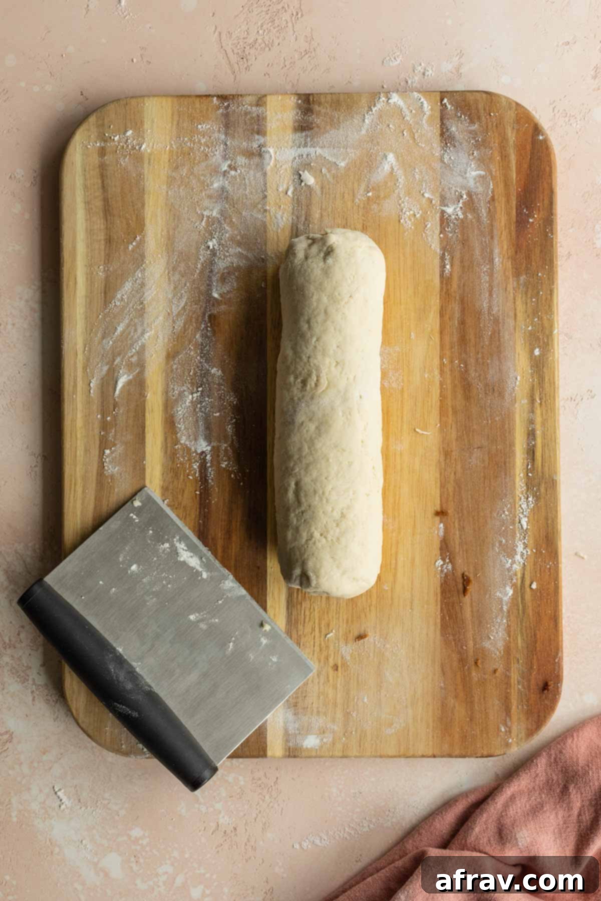 Cinnamon bun dough tightly rolled into a log on a wooden cutting board, ready for slicing.